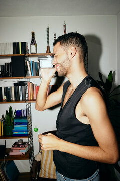 Side view of smiling young man filming through vintage video camera at home