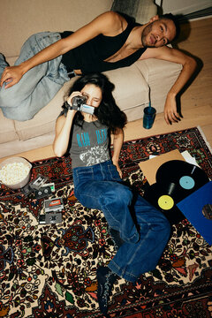 High angle view of woman filming through video camera while man lying on sofa at home