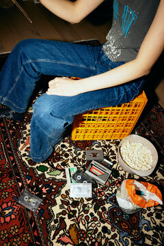 Low angle view of woman sitting on crate amidst audio cassettes and snacks over carpet at home