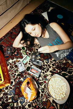 High angle view of woman checking audio cassette while lying on carpet at home