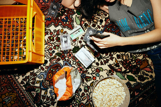 Midsection of woman holding audio cassette while lying on carpet at home