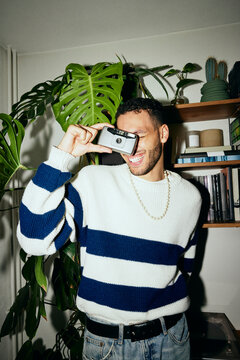 Portrait of happy young man clicking pictures through vintage camera at home