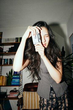 Young woman clicking pictures with film camera at home