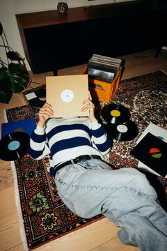 High angle view of young man covering face with vinyl cover while lying down on carpet at home