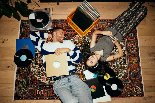 High angle view of friends spending leisure time while lying amidst vinyls on carpet at home