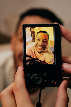 Hand of woman clicking picture of male friend through digital camera at home