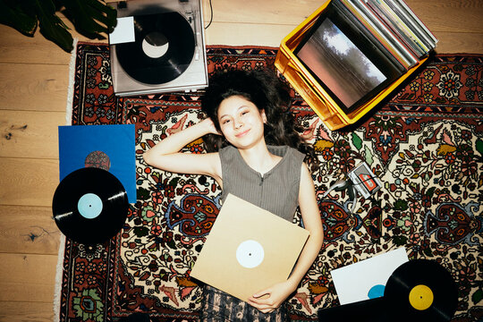 Directly above shot of smiling woman lying down with record vinyls on carpet at home