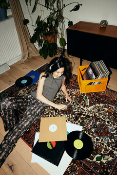 High angle view of woman listening to music on personal stereo while reclining on carpet at home