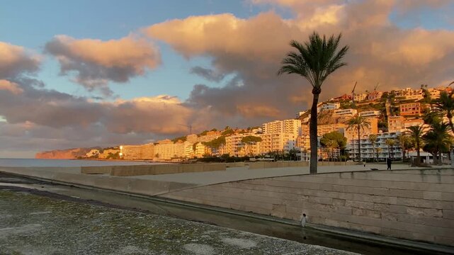 Tenfold accelerated movement of morning clouds against the backdrop of a beach and a canal draining water into the sea. Mallorca Island, Spain. Mediterranean Sea.