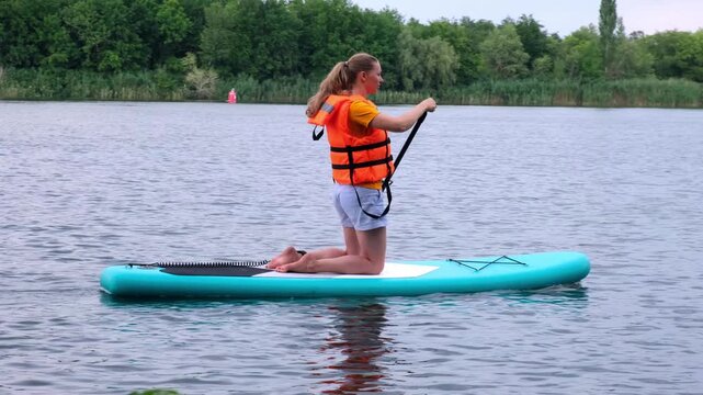 Woman kneeling on a stand up paddleboard on a lake outdoors. water sport, active leisure, summer vacation, nature fitness, calm water