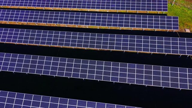 Multiple horizontal lines of photovoltaic modules creating a repetitive industrial texture. Geometric pattern of solar panel rows on dark ground. Aerial view.