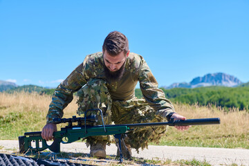Obraz premium Military Sniper Soldier Preparing Rifle in Open Field Landscape