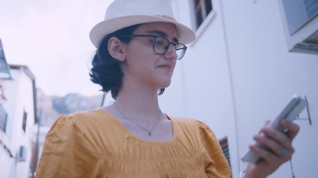Casual Young Woman in Hat Relaxing on Old European Street and Using Mobile Device