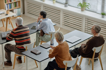 Group of middle aged and senior Caucasian men and women sitting at desks listening to instructor...