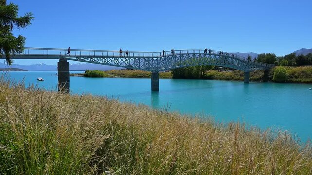 Eine Br&uuml;cke &uuml;ber einen See mit Menschen, umgeben von Bergen und dem klaren Himmel, Lake Tekapo, Tekapo, Canterbury, S&uuml;dinsel, Neuseeland, Ozeanien