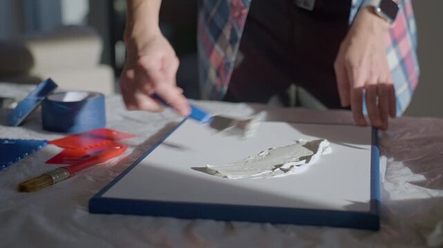 Woman applying textured paste on canvas using tools on work table in studio. Concept of textured art creation