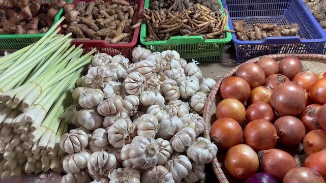 Vibrant display of fresh culinary ingredients at an outdoor market, featuring organic garlic bulbs, green lemongrass stalks, and colorful onions
