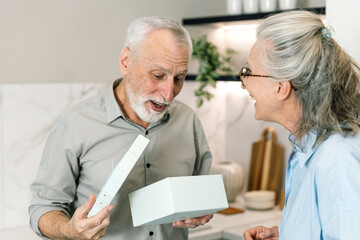 Fototapeta premium Elderly man opening a surprise gift from his wife at home