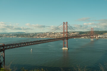 Obraz premium 25 de Abril Bridge in Lisbon, Portugal - a stunning, 2,277-meter-long suspension bridge that bears a striking resemblance to San Francisco's Golden Gate Bridge on a sunny day 