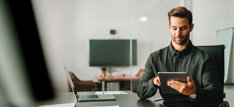 Executive professional man working online using computer for financial business banking work. European trade manager looking at digital tablet screen sitting at desk in office. Web banner, copy space