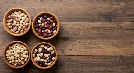 Four small wooden bowls filled with various types of dried beans arranged on a rustic wooden table surface