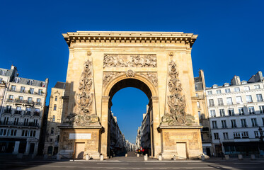Obraz premium Scenic sunny view of the historic Porte Saint-Denis triumphal arch with intricate bas-relief carvings and classical Parisian buildings in Paris, France.