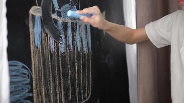 Focused little boy drawing with blue chalk on a blackboard at home or in classroom. Early education, creativity and childhood development concept. Side view portrait with copy space
