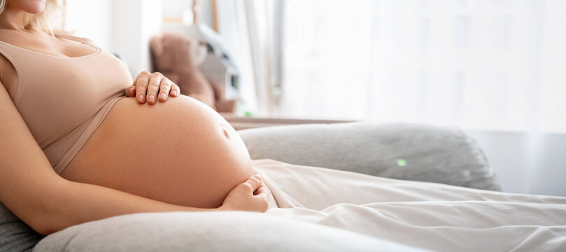 Closeup belly at third trimester. Future mother woman touching naked tummy, doing massaging lying with love in bed in bedroom at home. Pregnant eco, prenatal, maternity concept. Web banner, copy space