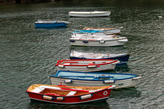 A picturesque view of vibrant, multi-colored wooden boats moored in the tranquil harbor of Puerto de Tapia de Casariego, Asturias. The image captures the authentic maritime atmosphere