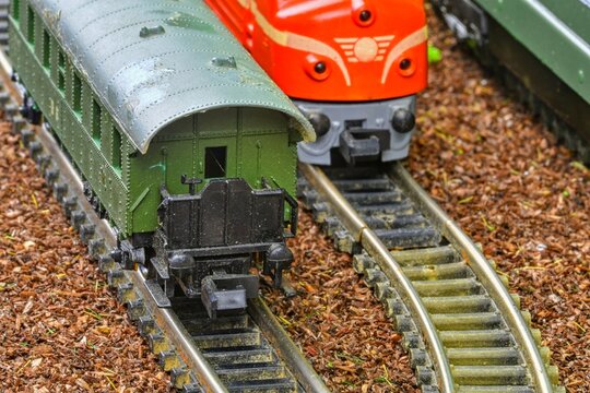 Close-up of two miniature train cars on a model railway track with wooden ballast. Detailed view of a green passenger car and a red locomotive on a curved track, showcasing intricate model railway