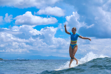 Obraz premium Female Surfer Celebrating Victory On Wave Crest, Arms Raised And Radiant Smile, Sunlit Ocean And Dramatic