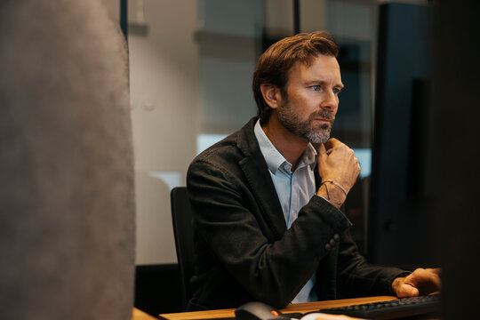 Serious male entrepreneur working on computer while sitting at desk in office