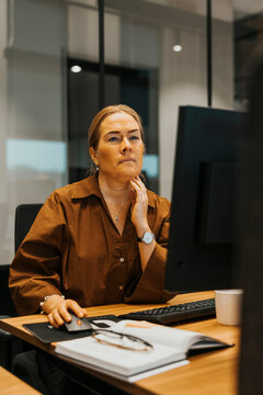 Thoughtful mature businesswoman working on computer while sitting at desk in modern office