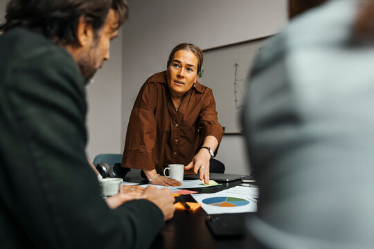 Mature businesswoman discussing over documents with colleagues in meeting at office