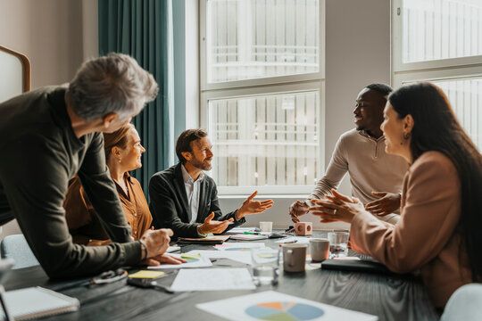 Team of smiling business professionals discussing ideas while sitting around table in meeting room