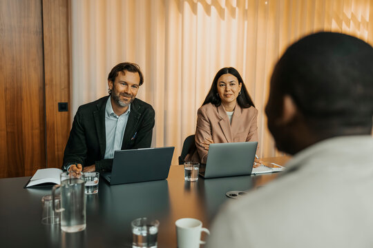 Smiling male and female entrepreneurs taking interview of candidate in office board room