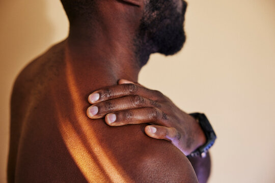Shirtless man touching his stiff shoulder against colored background