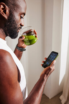 Concentrated man drinking healthy juice while examining body scan data on smart phone