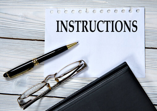 INSTRUCTIONS - word in white paper on the background of a diary, glasses and pen