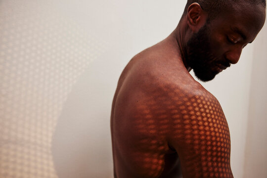 Patterned shadow of sunlight shining on shirtless man