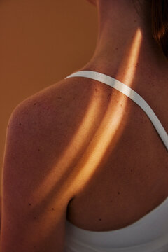 Rear view of sunlight ray shining on woman's shoulder wearing sports bra