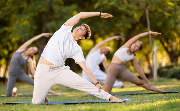 During street workout, yoga practice on lawn in public park, people with guy teacher work with bodies do carry out bolt pose exercise. Youth attend outdoor yoga lesson in park