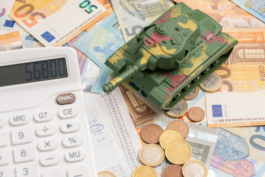 Toy tank on money and coins near calculator and cash receipt