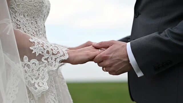 A Symbol of Commitment: Close-up of bride and groom hands holding, displaying gold wedding rings for marriage and relationship projects.