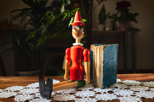 Classic fairy tale wooden puppet of pinocchio sitting next to an old book, evoking themes of lies and stories