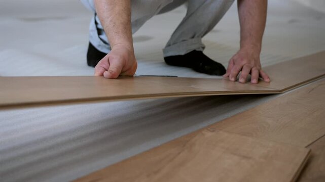 Worker aligning and clicking laminate floor panels together. Interior renovation and flooring installation process.