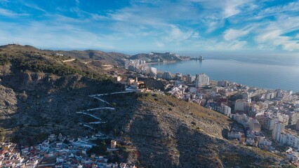 Obraz premium Wide aerial panorama of Cullera in Spain showing the Mediterranean coastline, river mouth and mountain ridge. Detailed drone view of seaside city, beaches and surrounding landscape.