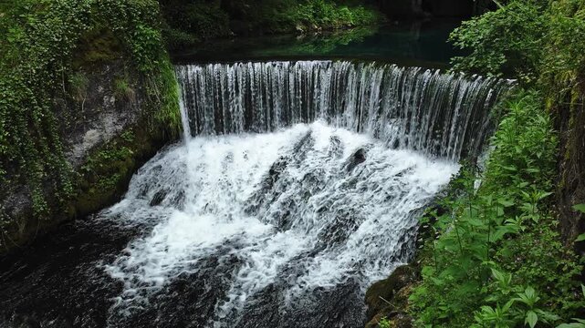 Small waterfall in lush green forest with clear freshwater flowing over rocks. Natural cascade surrounded by vegetation in peaceful Serbian landscape