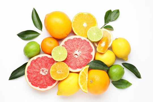 Different fresh citrus fruits and green leaves on white background, flat lay