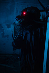 Fototapeta premium Scary Halloween Monster Costume with Glowing Red Eyes in Dark Abandoned Building